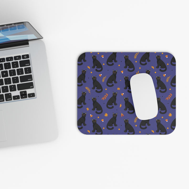 Mouse pad with black cat pattern next to a laptop on a white surface