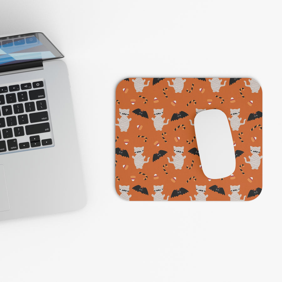 Orange mouse pad with cat and bat pattern next to a laptop on a white surface