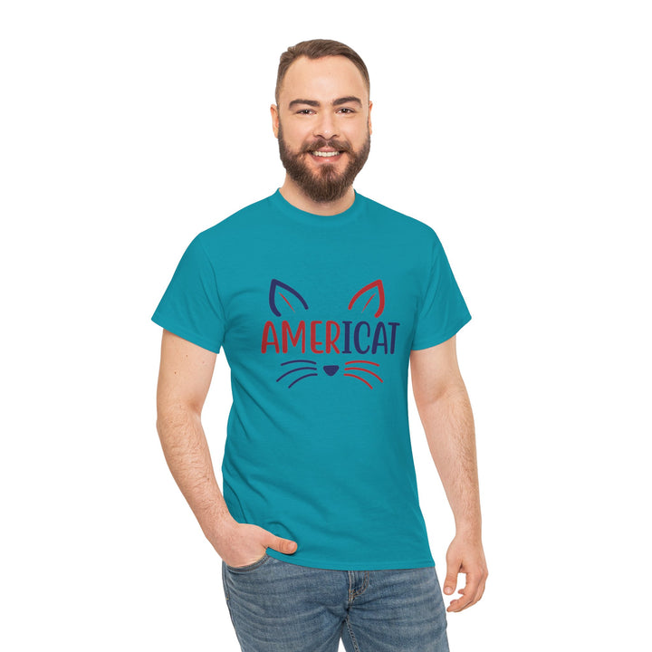 A man with a beard wearing a teal t-shirt with a 'AMERICAT' cat graphic, paired with blue jeans, standing against a plain white background.