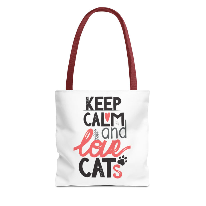 A white canvas tote bag with dark red shoulder straps, featuring the printed text 'KEEP CALM and love CATS' in black and coral pink lettering on the front, set against a plain white background.