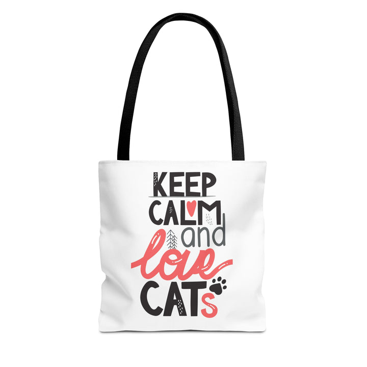 A white canvas tote bag with black shoulder straps, featuring a printed graphic on the front that reads 'KEEP CALM and love CATS' in black and coral pink lettering with small cat-themed illustrations.