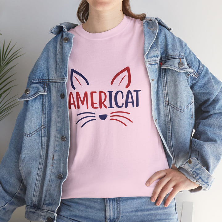 A person wearing a light pink crewneck t-shirt with a 'AMERICAT' cat face graphic in red and navy blue, styled with an open light-wash denim jacket.
