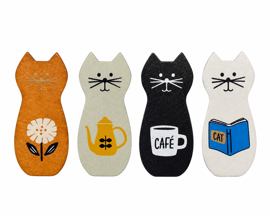 Four cat-shaped wooden coasters or trivet pads in orange, cream, black, and white, each decorated with a different illustration (a flower, a teapot, a coffee cup reading 'CAFE', and a blue book reading 'CAT').