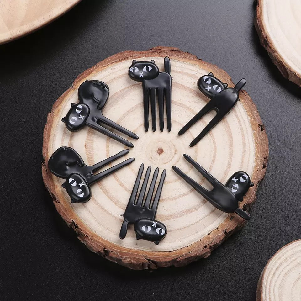 Black cat-shaped fruit picks arranged in a circular pattern on a wooden surface.