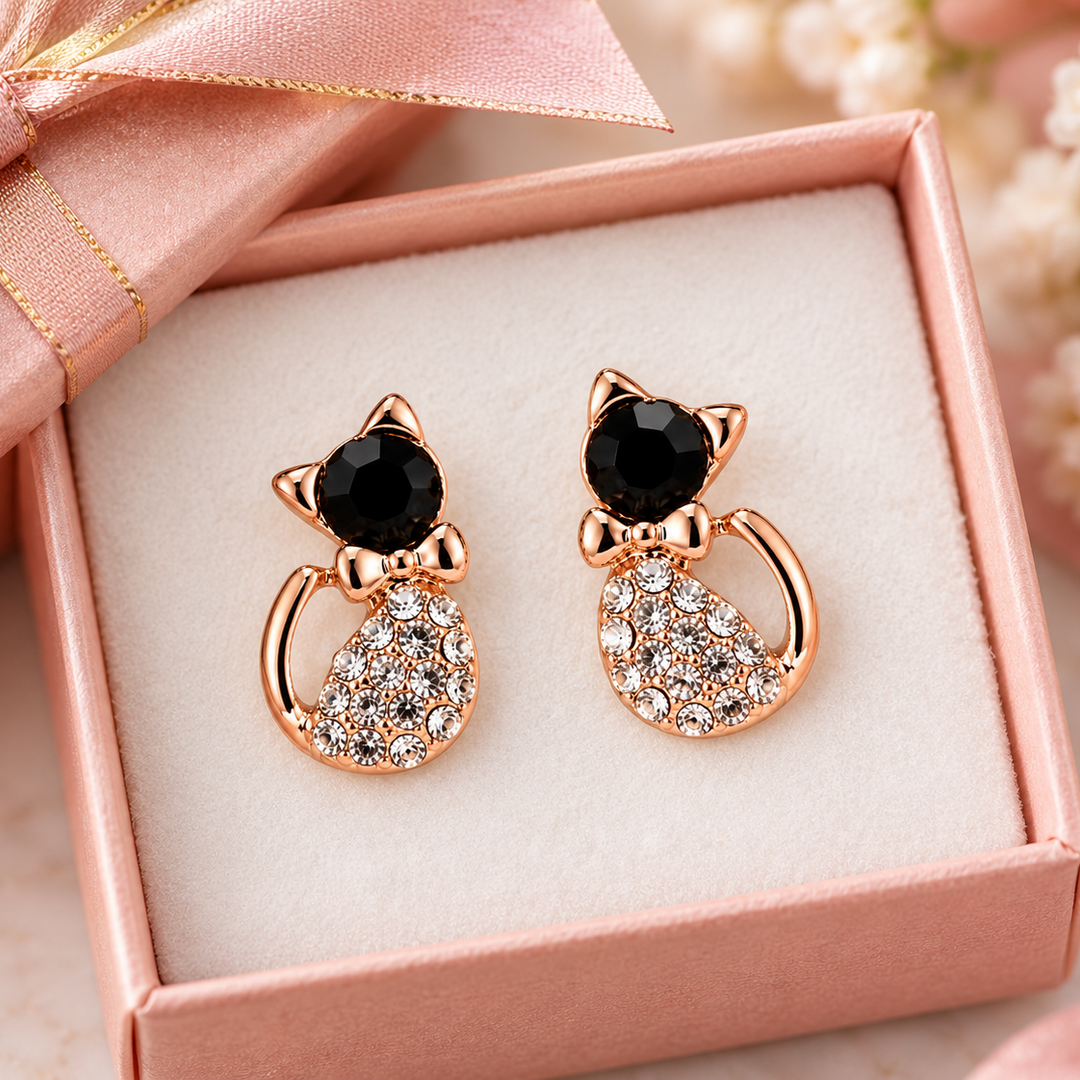 A pair of rose gold cat-shaped stud earrings with black faceted gemstones and clear rhinestone accents, presented in a pink gift box with a pink satin ribbon.