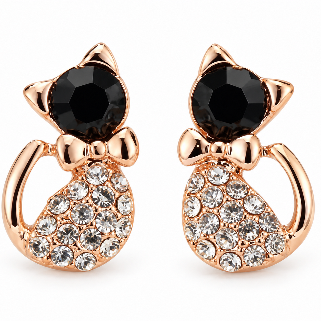 A pair of rose gold cat-shaped stud earrings featuring a faceted black gemstone for the head, a small bow detail, and a body paved with clear round crystals, set against a plain white background.