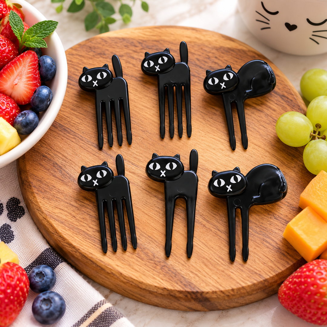 Six black cat-shaped cheese picks arranged on a round wooden board, surrounded by strawberries, blueberries, grapes, cheese, mint, and a white ceramic cup with a cat face.