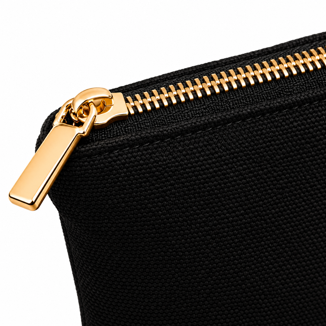 Close-up of a black canvas zippered pouch with a shiny gold zipper and pull tab, set against a plain white background.