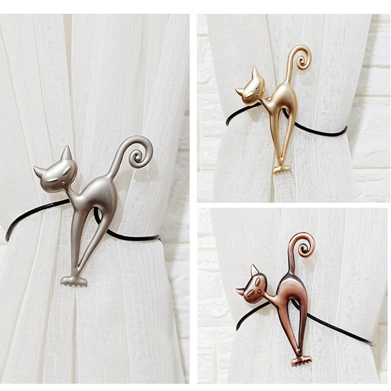 Three cat-shaped curtain tiebacks in silver, gold, and bronze on a white curtain background.